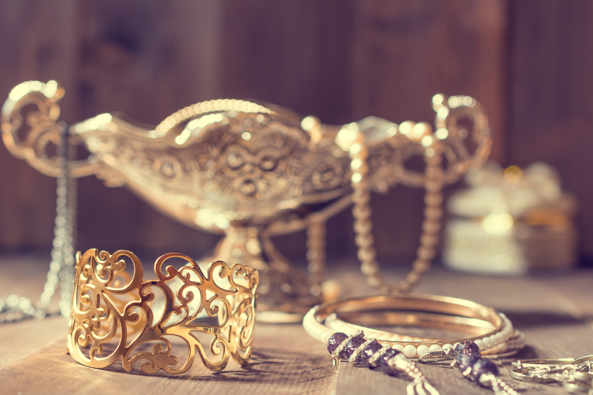 Vintage golden bracelet and silver vase with jewelry on wooden background